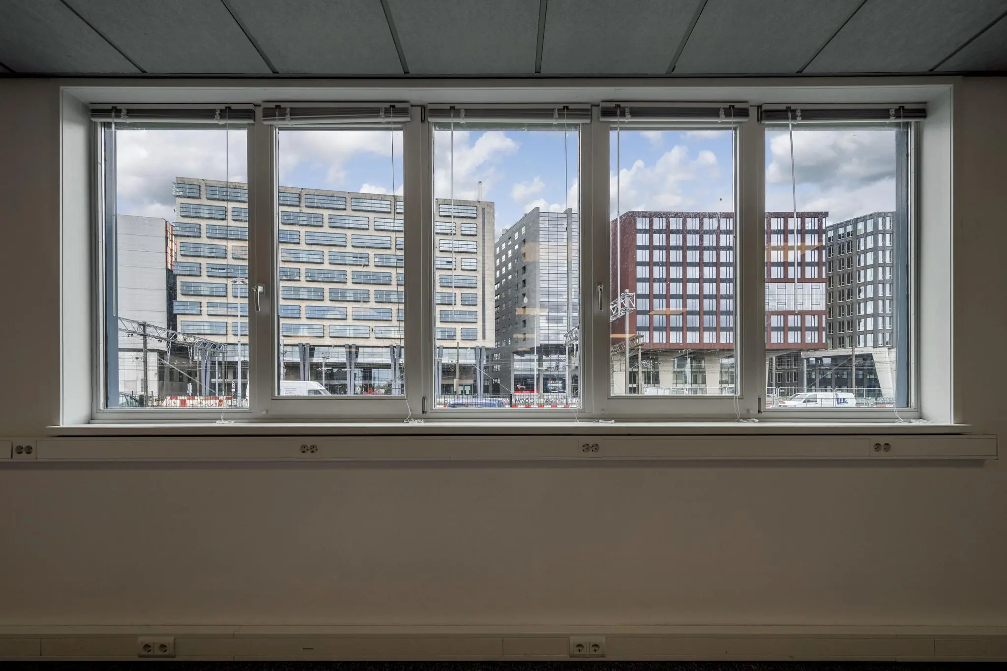 Uitzicht vanaf binnenkant van een gebouw aan de De Ruijterkade op moderne kantoren en hoge gebouwen.